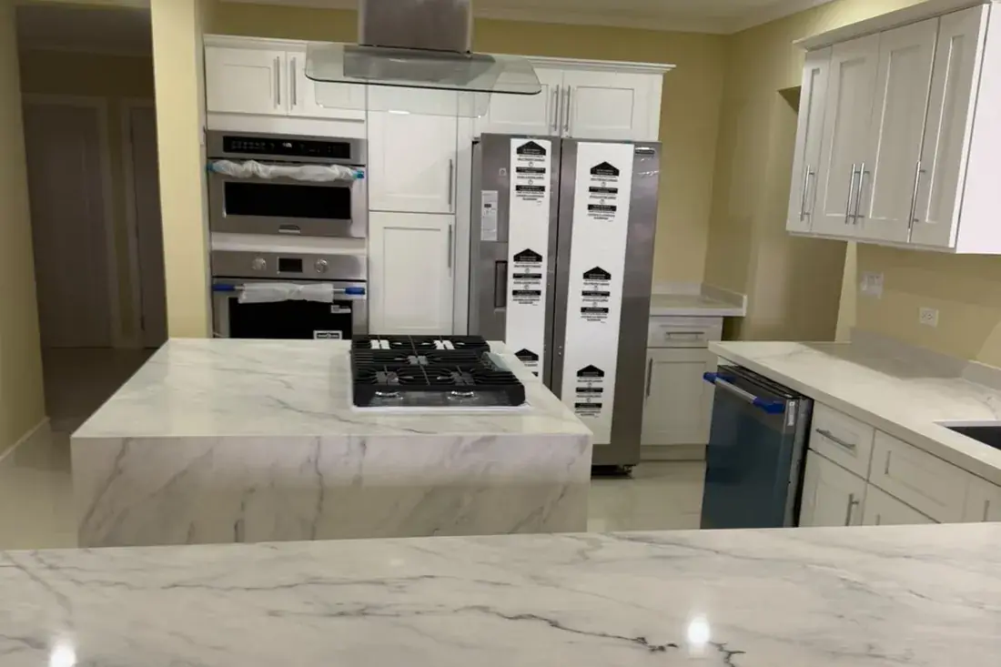 The same kitchen built, with marble counters, the gas hob in the island and the ovens beside the fridge