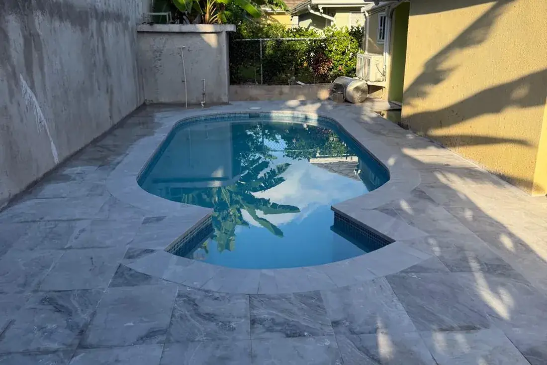 The same pool finished, filled and running, ringed by a marble tiled surround