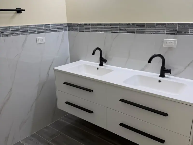 A bathroom with a twin wall hung vanity, black taps and marble tiling with a banded border