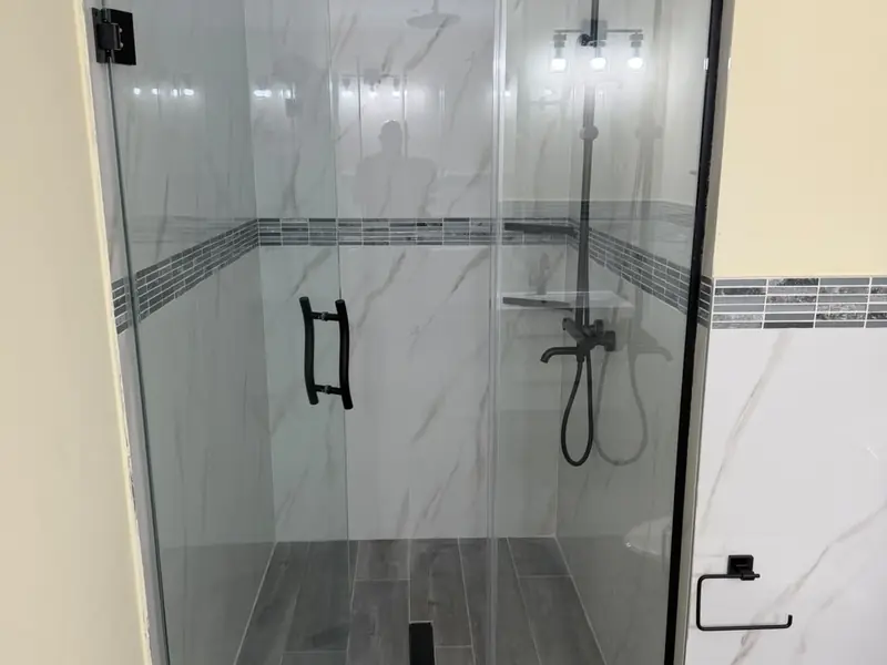 A walk in shower with black framed glass, a rain head and large format tiling