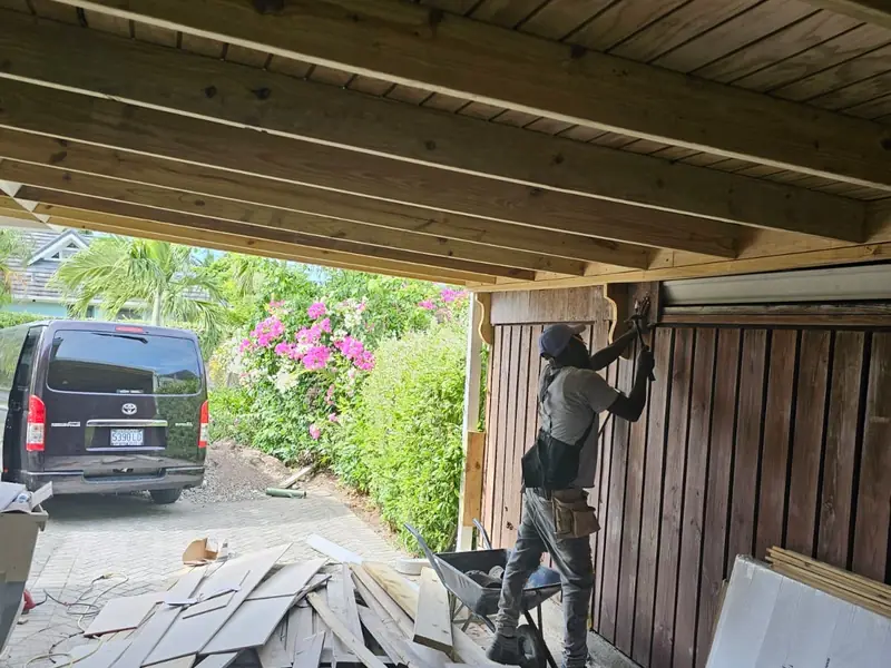 A carport with a new timber ceiling and a worker fitting vertical timber cladding to the wall