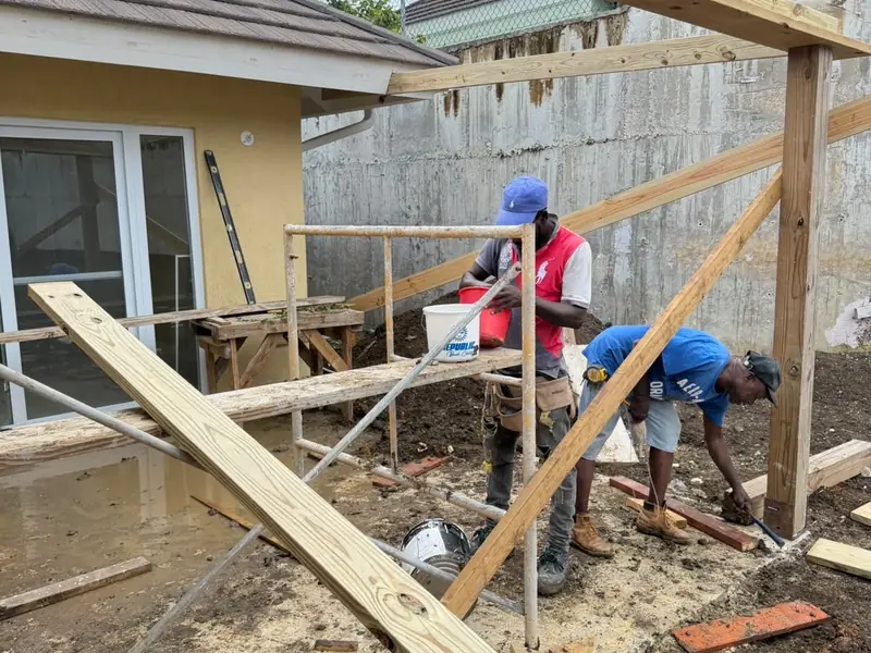 Two workers setting timber formwork and bracing for an addition beside a finished house