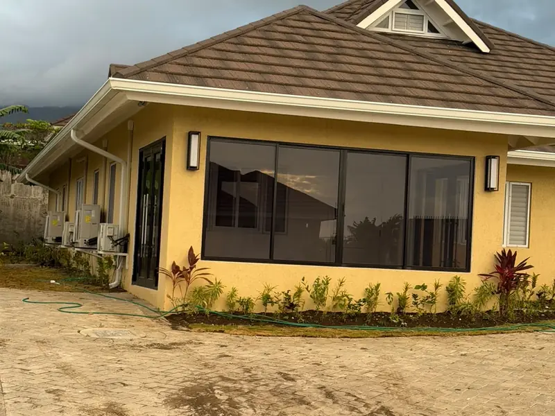 A finished yellow house with a bay window, planted borders and a hipped roof