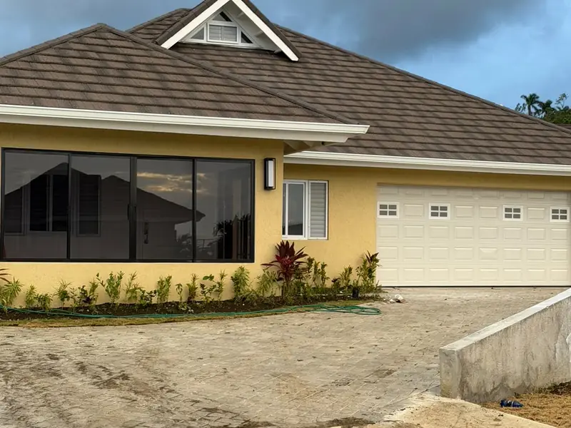 A finished yellow house with a garage, hipped roof and the driveway ground formed