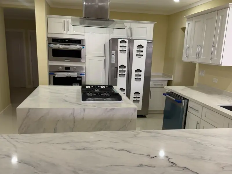 The finished kitchen with marble counters, a gas hob in the island, stainless extractor and built in ovens