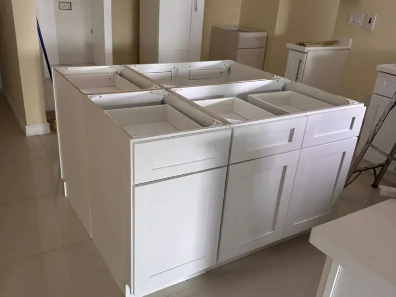 White kitchen base units and island carcasses standing on a tiled floor before any counters
