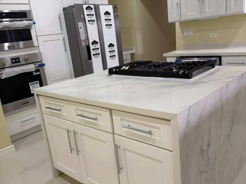 A kitchen island with a gas hob and extractor above, wall ovens and a fridge behind