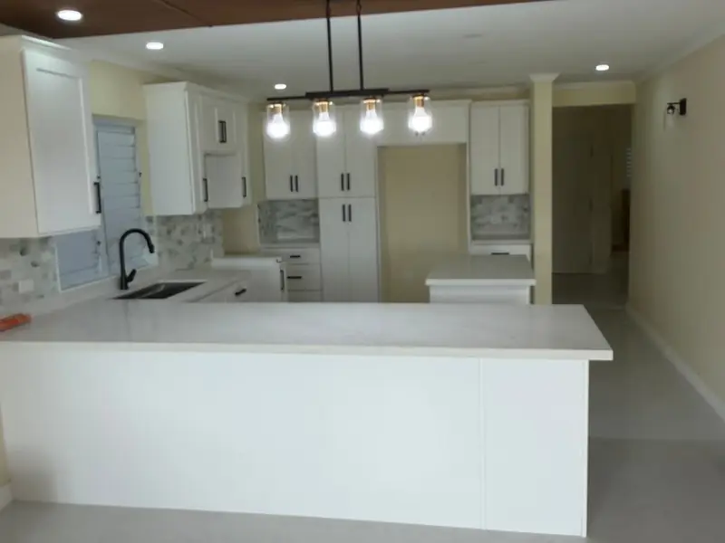 An open plan kitchen with a white island, pendant lights and a wall of tall units