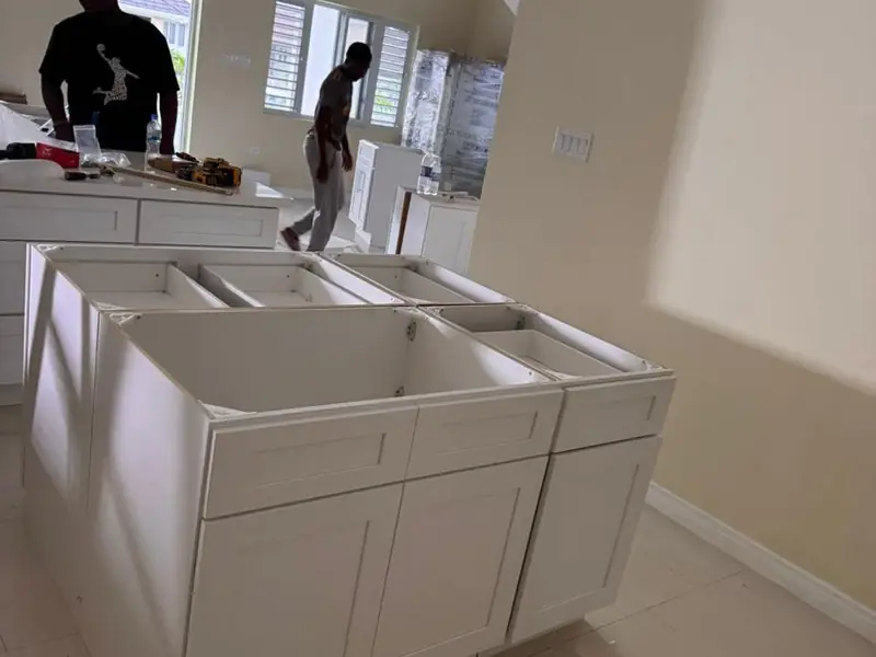 White kitchen base units and island carcasses set out on a tiled floor with two workers behind