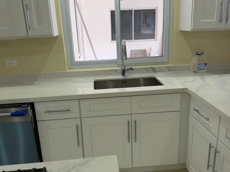 A kitchen corner with an undermount sink under a window, marble counter and a gas hob