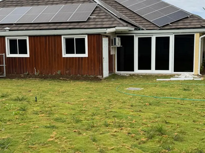 A wide view of the rear of a finished house with solar panels, timber cladding and a lawn