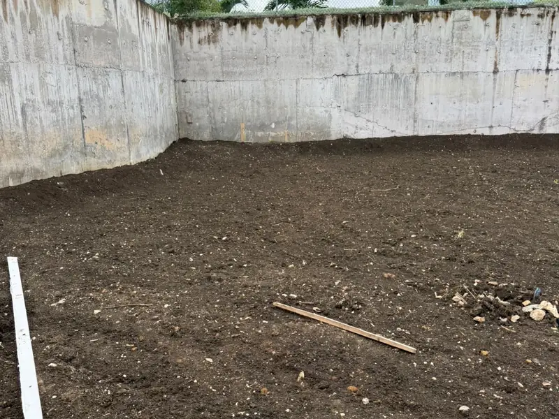 A levelled plot behind a curved block retaining wall with houses beyond