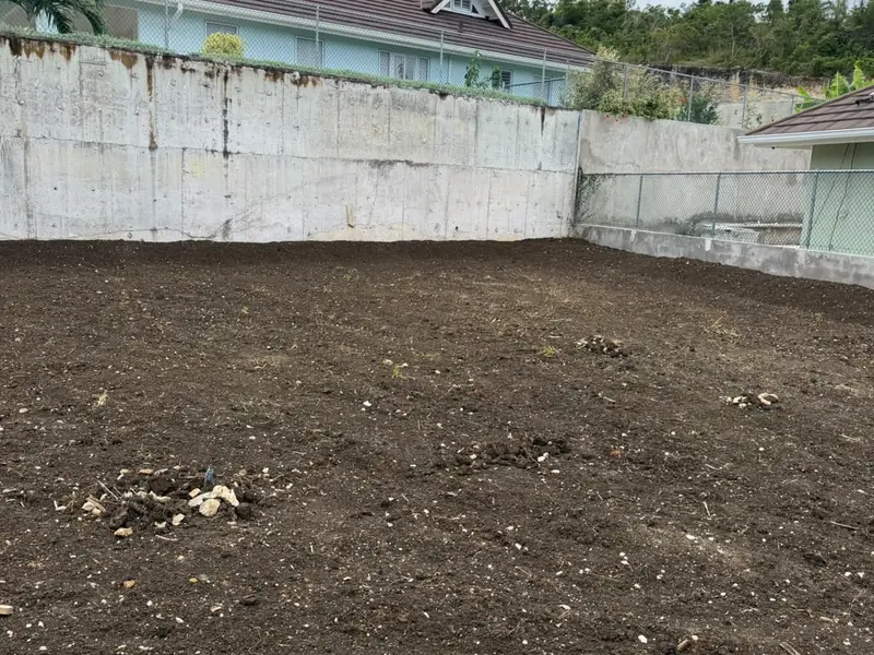 A cleared and levelled plot of dark earth behind a new block retaining wall
