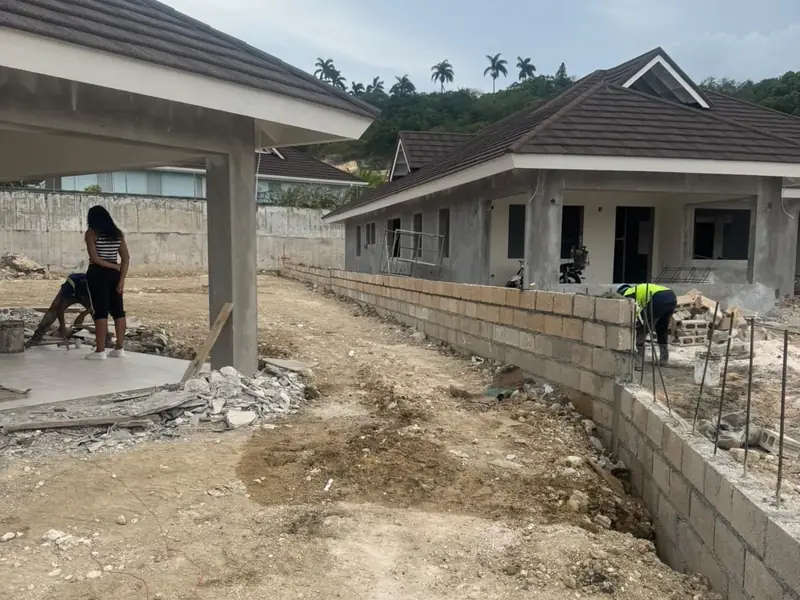 Houses under construction on a terraced site with a block retaining wall and workers on the ground