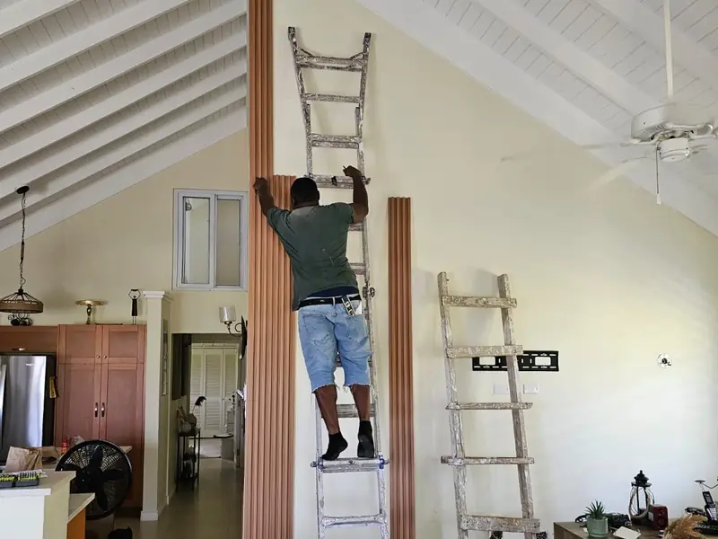 A worker on a ladder fixing vertical timber slats to a tall feature wall under a vaulted ceiling