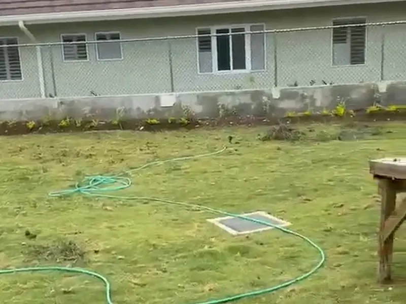 The rear of a finished house across a newly laid lawn, with a work bench and hose on the grass