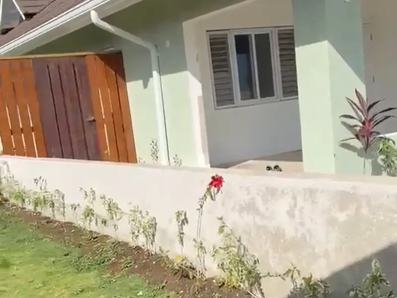 A finished pale green house with a car porch, seen across a flagstone driveway
