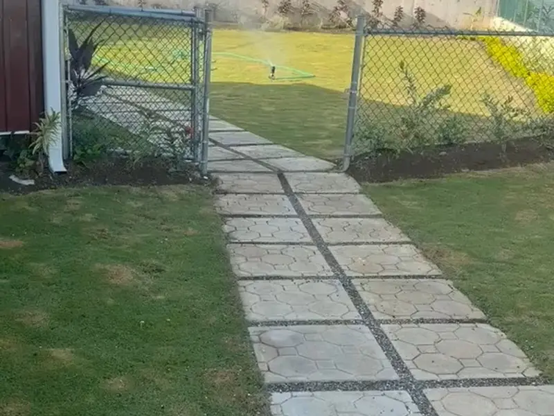 A paved walkway running between a lawn and a rendered boundary wall to a gate