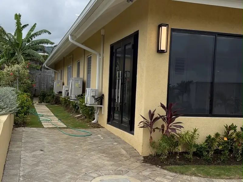 A paved walkway running along the side of a finished house with planting and glazed doors