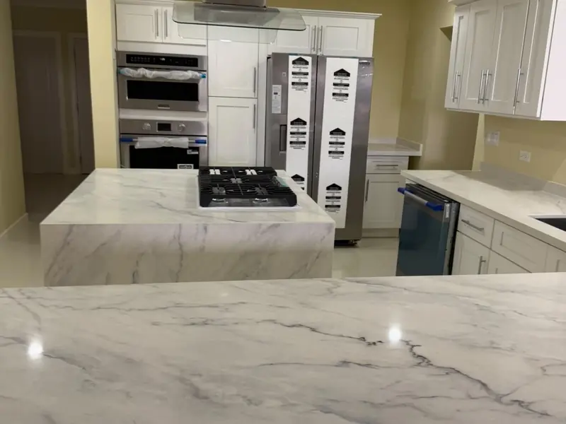 A kitchen with a marble worktop, built in wall ovens and an extractor hood