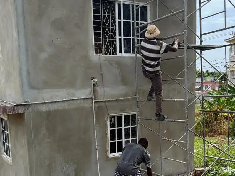 Two workers on a scaffold rendering the wall of a two storey house