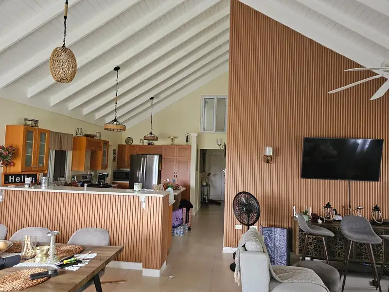 A living and dining room with a full height timber slat feature wall and a vaulted white ceiling