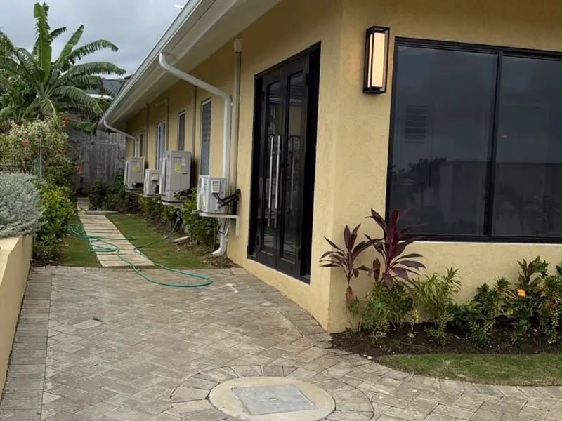 A paved walkway running along the side of a finished house with planting