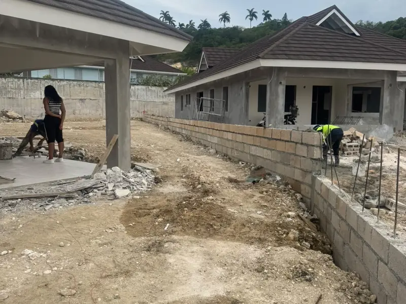 A house under construction with the roof on and a worker on the ground works